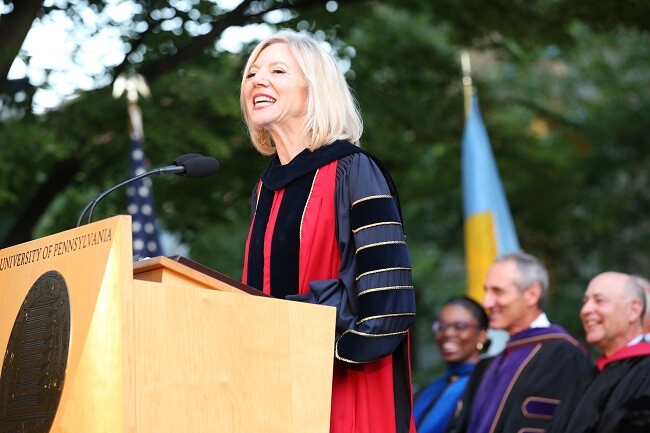 Amy Gutmann speaking at podium in wearing blue and red regalia
