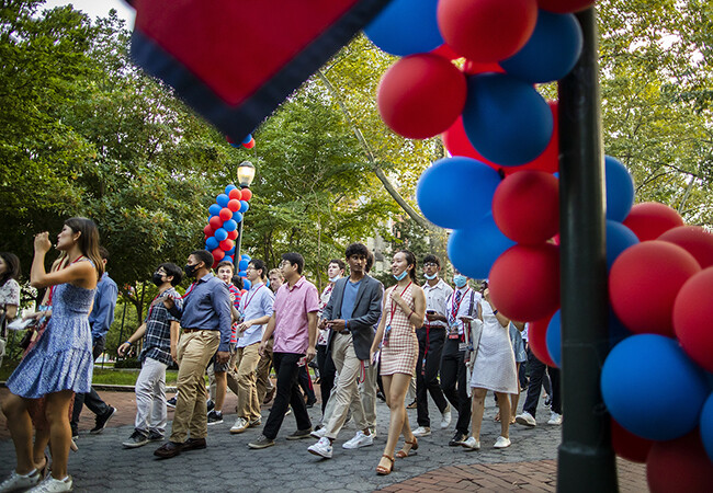students processional on Locust Walk past flags and balloon arches