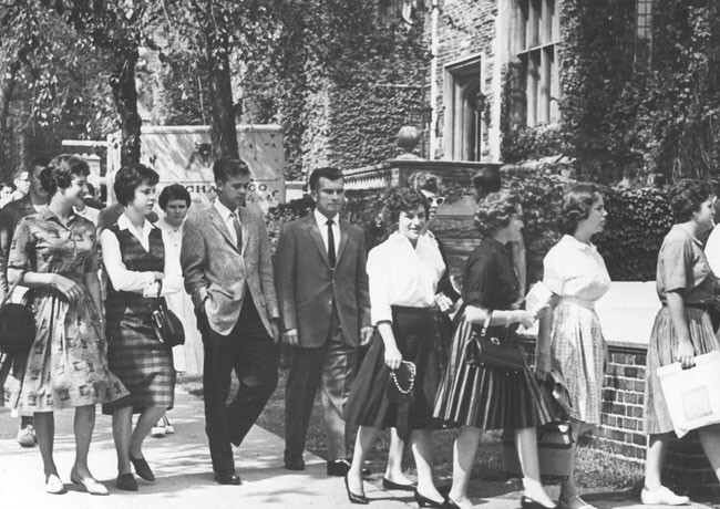 black and white 1960s photo of well-dressed students walking on sidewalk